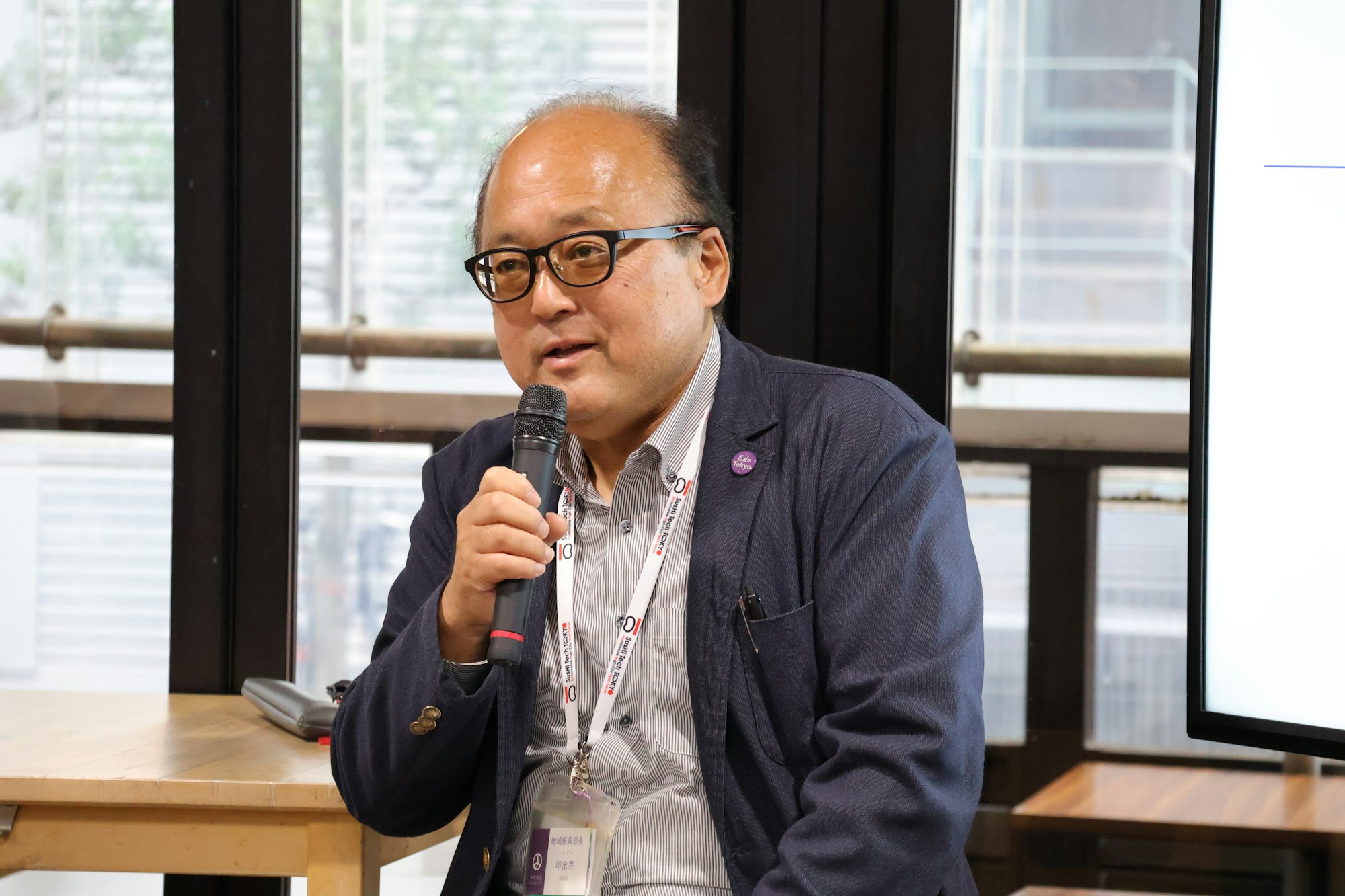 千代田区役所　地域振興部長　印出井 一美氏がマイクを手に登壇している写真